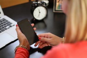 woman's hand holding phone with analog alarm clock in background with a time of 7:00 feeling overwhelmed